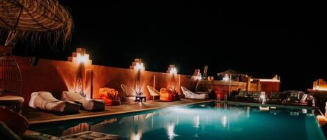 A nighttime pool area with lounge chairs and umbrellas, surrounded by walls with built-in lighting.