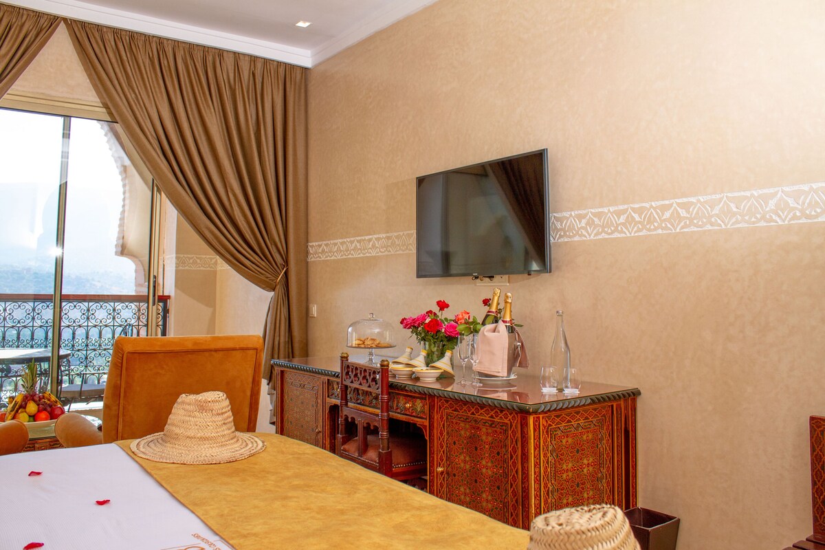 A hotel room with a bed, a desk with a vase of flowers, a television, and a balcony with a view.