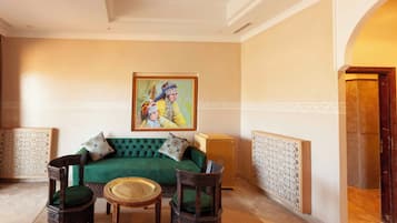 Una habitación con un sofá verde, dos sillas de madera, una mesa redonda pequeña y un cuadro en la pared.