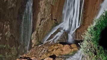 A waterfall cascading over rocky terrain with moss-covered rocks and a small stream at the base.