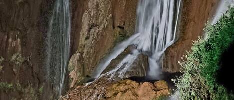 A waterfall cascading over rocky terrain with moss-covered rocks and a small stream at the base.