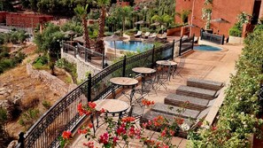 Un espace piscine aménagé sur le toit, avec des chaises longues et des tables, entouré d’une rambarde en métal et d’une végétation luxuriante.
