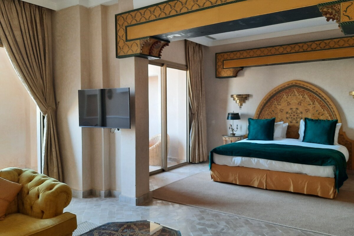 A hotel room with a bed, a television, a sofa, and a patterned rug.