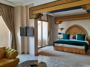 A hotel room with a bed, a television, a sofa, and a patterned rug. - Borj Des Cascades & Spa (Ait Taguella)