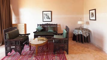 A traditional room with a sofa, two armchairs, a small round table, a patterned rug, and a lamp.