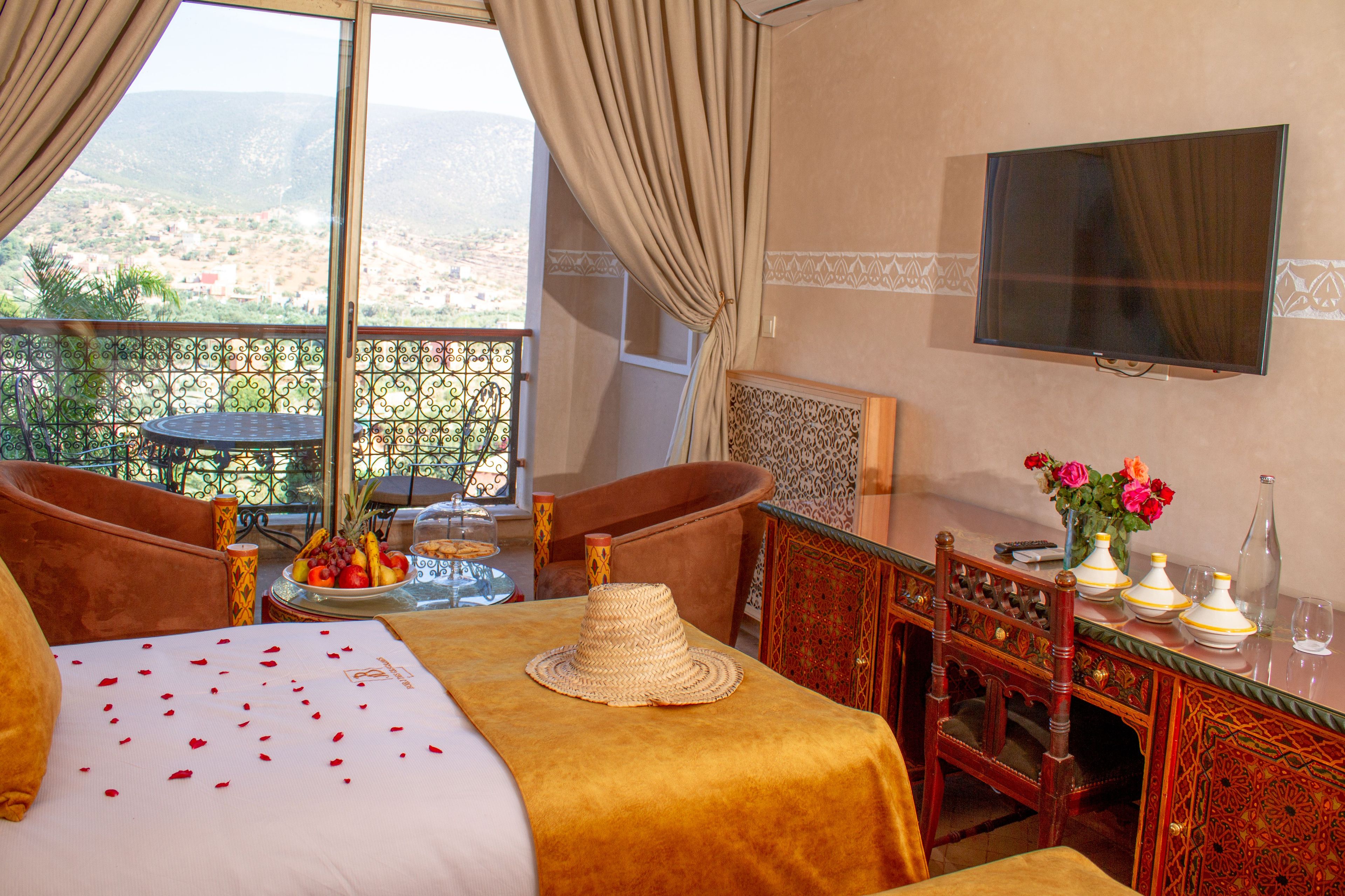 Habitación de hotel con cama, una mesa de comedor con un florero y televisión montada en la pared, con vista a la ciudad a través de la ventana.