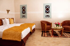 A hotel room with two beds, a sitting area with a sofa and a small table, and decorative wall sconces. - Borj Des Cascades & Spa (Ait Taguella)