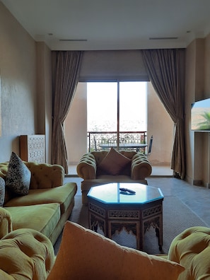 A living room with a sofa, a coffee table, and a balcony with a view. - Borj Des Cascades & Spa (Ait Taguella)