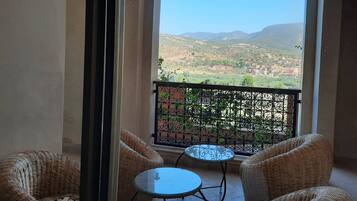 Un balcón con mobiliario de mimbre y una mesa de vidrio, con vistas a un paisaje montañoso.