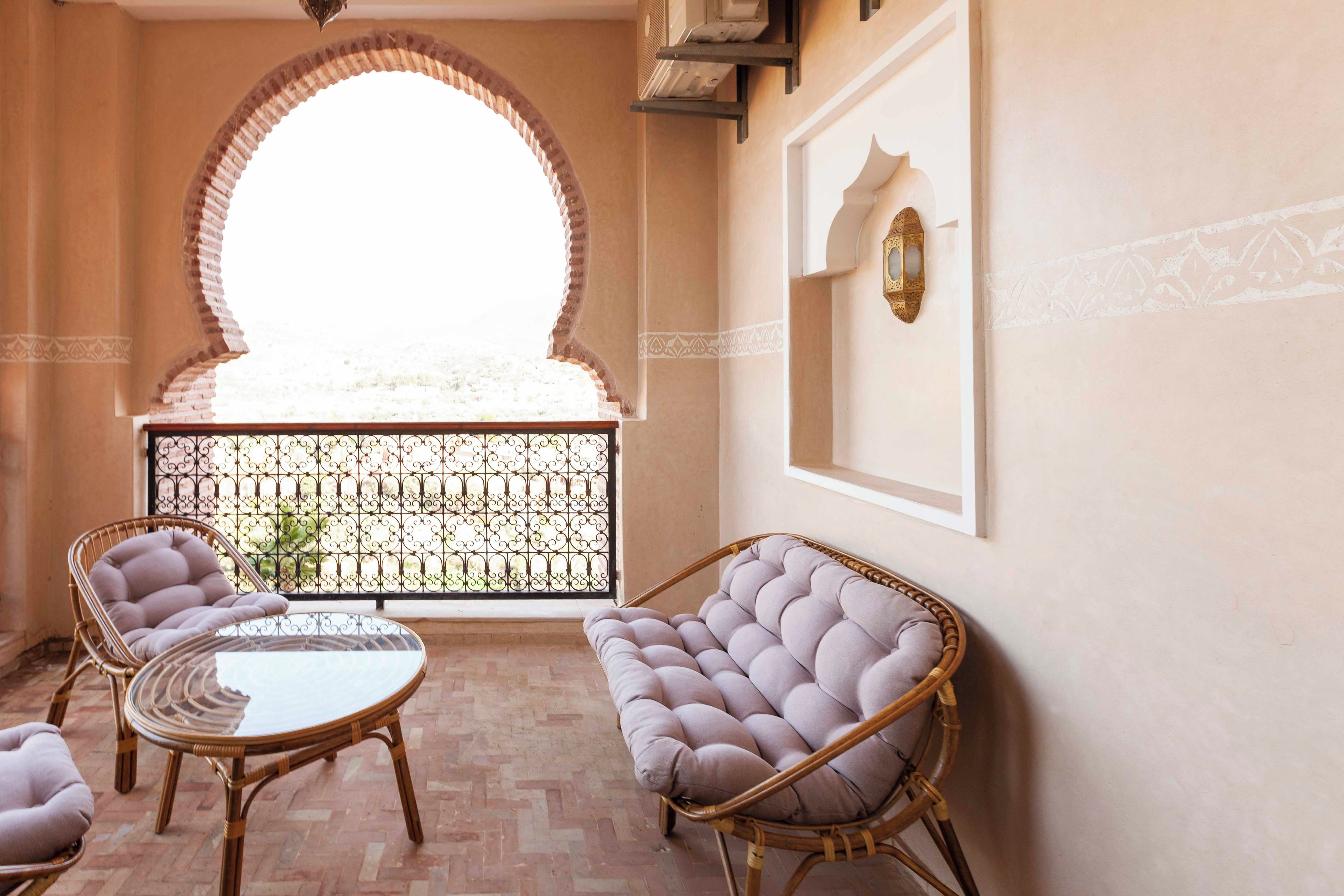 A balcony with wicker furniture, a glass table, and a view through a wrought iron gate.