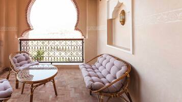 A balcony with wicker furniture, a glass table, and a view through a wrought iron gate.