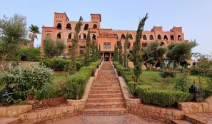 Ein Gebäude mit einer zentralen Treppe, die zu einer Tür führt, umgeben von gepflegten Gärten und Bäumen.