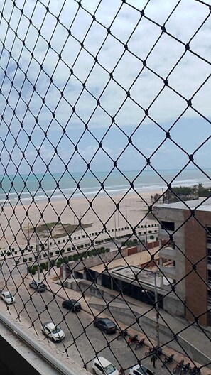 A chain-link fence with a view of a beach and buildings in the background. - Apê Pé na Areia-Vista Mar (Fortaleza)