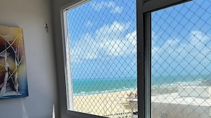 Ein Zimmer mit großem Fenster mit Blick auf einen Strand, einem Holztisch und einem Stuhl.