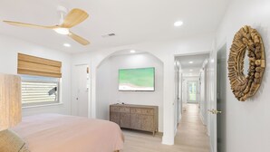 Ein Schlafzimmer mit Bett, Deckenventilator, Schminktisch und einem Flur, der in einen anderen Raum führt.