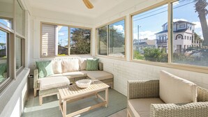 Ein Wintergarten mit großem Fenster, Deckenventilator, Sofa, Couchtisch und Korbmöbeln.