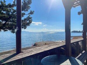Una terraza de madera con vistas a un cuerpo de agua y montañas distantes, cielo despejado y una estructura de mirador.