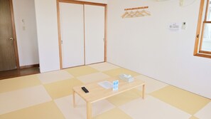 Een kamer met tatami vloermatten, een houten tafel met een afstandsbediening en een zakdoos, een schuifdeur en een wandkapstok.