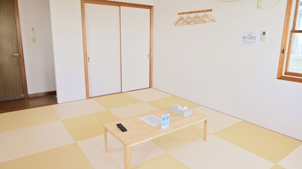 Een kamer met tatami vloermatten, een houten tafel met een afstandsbediening en een zakdoos, een schuifdeur en een wandkapstok.