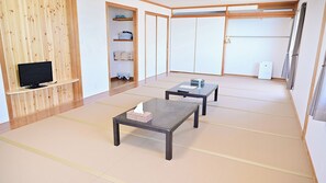 A room with tatami flooring, a television on a wooden shelf, two tables with baskets, and a wardrobe with sliding doors.