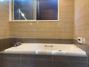 Un baño moderno con una bañera grande, una ventana con persianas y un perchero.