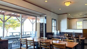 An indoor dining area with tables and chairs, large windows, and a view of the outdoors.