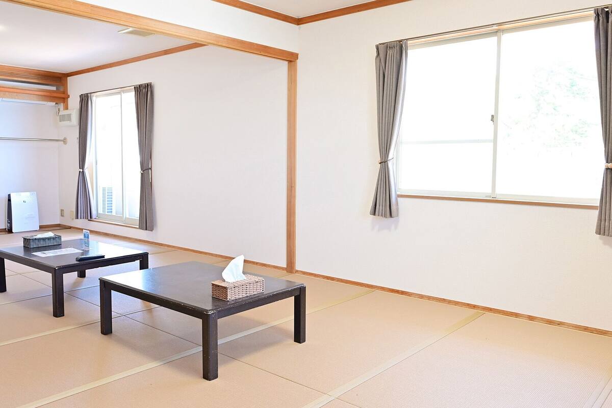 Ein Zimmer mit zwei Tischen, einem fensterbepften Fenster und einer weißen Wand.
