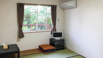 A room with a window, a television on a stand, a small table with a tissue box, and a futon with cushions.
