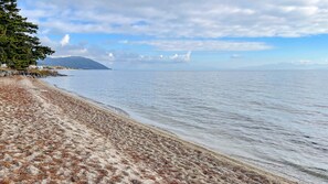 Une plage bordée d’un rivage rocheux, une montagne à l’horizon et un ciel dégagé.