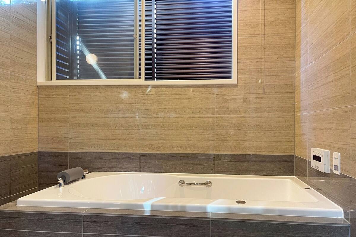 Ein modernes Badezimmer mit einer großen Badewanne, einem Fenster mit Jalousien und einem Handtuchhalter.