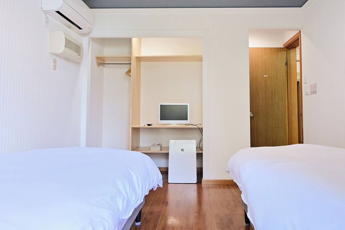 Ein Hotelzimmer mit zwei Betten, einem Schreibtisch mit Computer, einem Kleiderschrank und einer Klimaanlage.