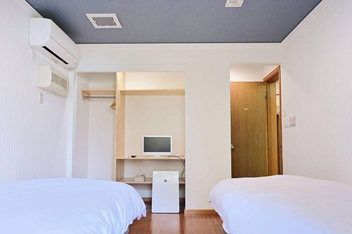 Ein Schlafzimmer mit zwei Betten, einem Schreibtisch mit Computer, einem Kleiderschrank und einer Tür zu einem anderen Raum.
