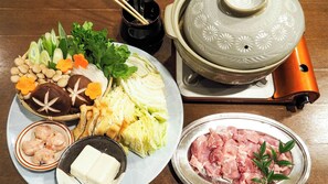 A traditional Japanese meal setup with various dishes including vegetables, tofu, and meat, accompanied by a teapot and chopsticks.