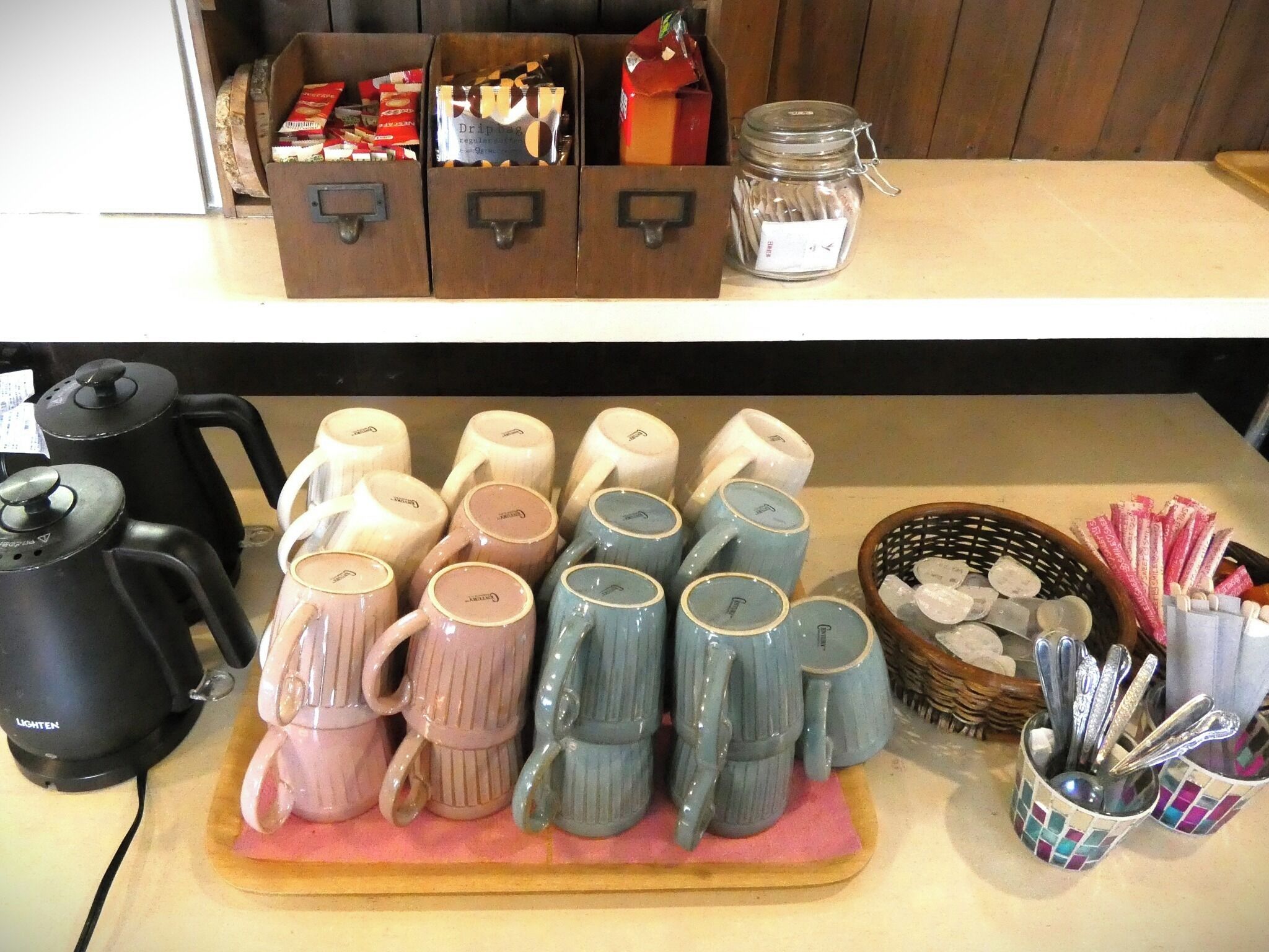 A kitchen counter with various mugs, a coffee maker, and a basket with utensils.