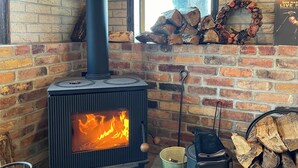 A wood-burning stove with a fire, a brick wall, and a window. - B B Dylan (Otsu)