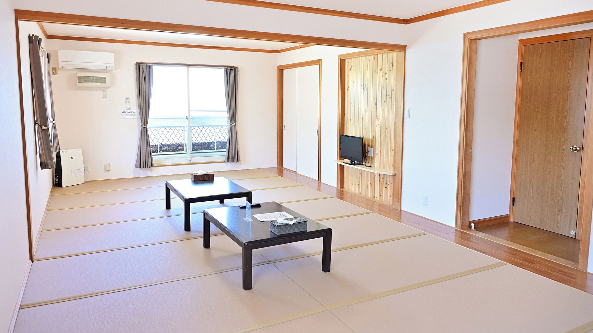 A room with tatami flooring, a sliding door, a television on a wooden shelf, and a window with curtains.