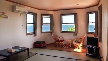 A room with a view of the sea, a television, and a futon bed.