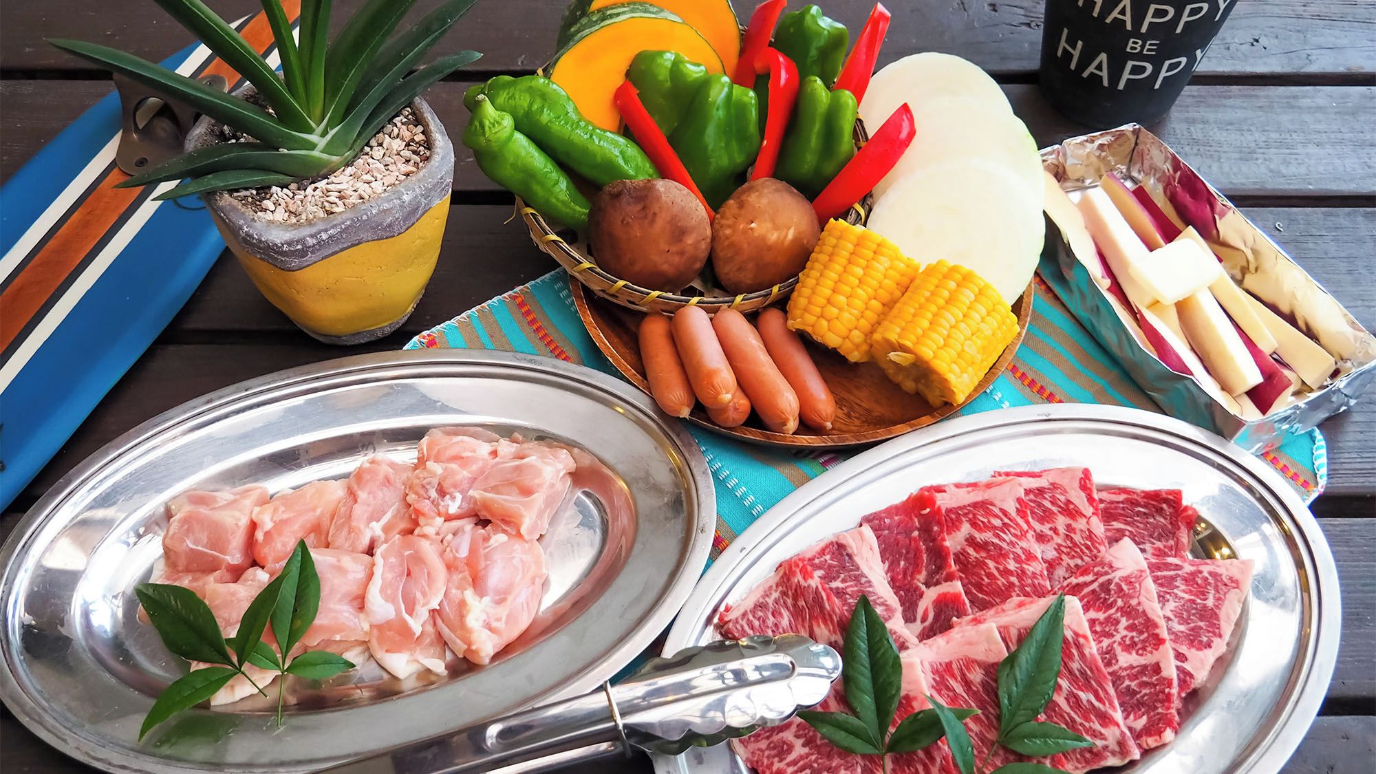 A table with various food items including raw chicken, steak, vegetables, and sausages.