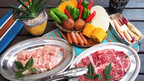 Een tafel met diverse etenswaren, zoals rauw vlees, steak, groenten en worst.