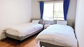 A room with two single beds, a window with curtains, a bedside table, and a nightstand.