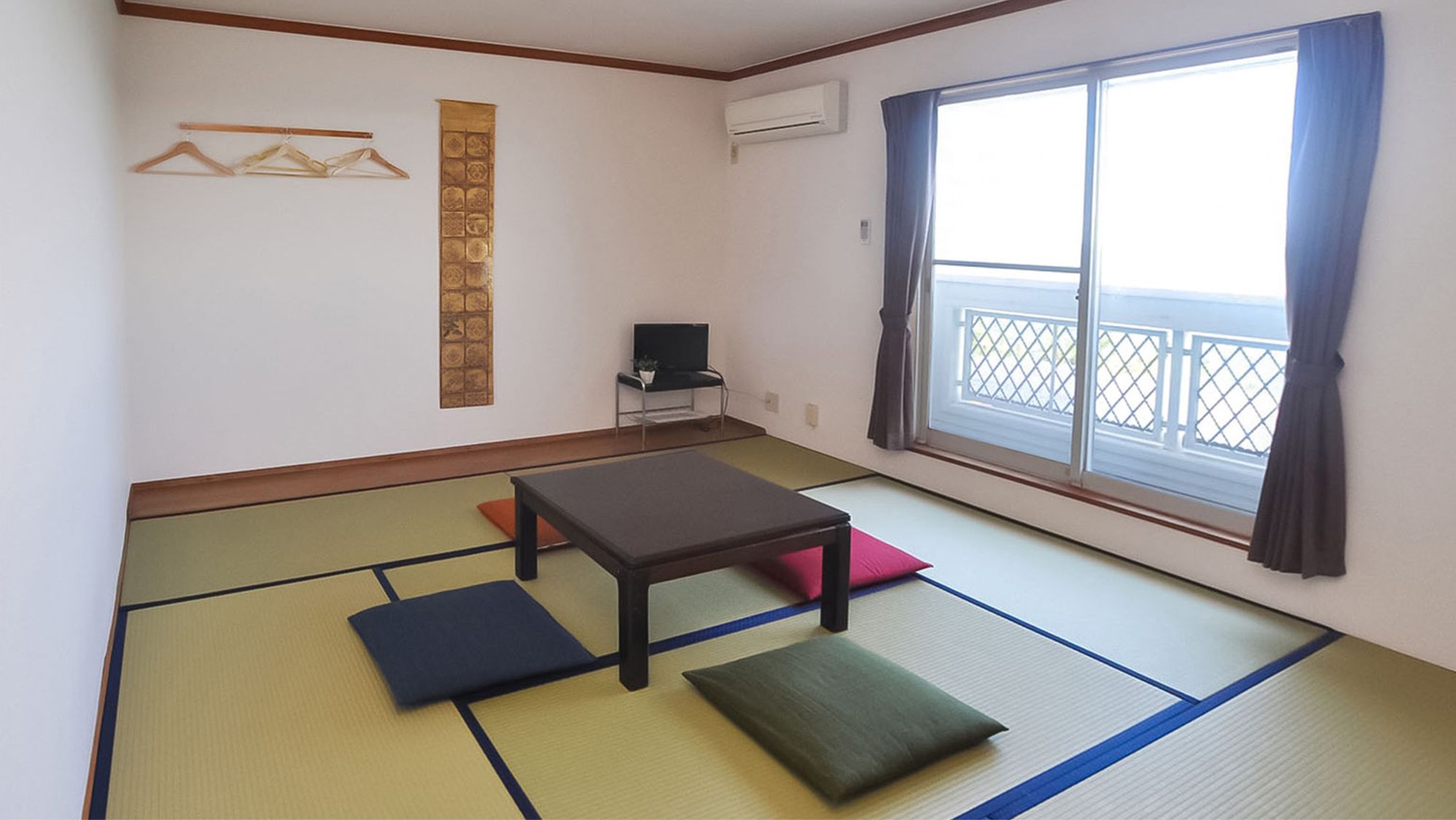 Una habitación con suelo de tatami, una mesa baja, cojines, un televisor y una ventana con vistas.