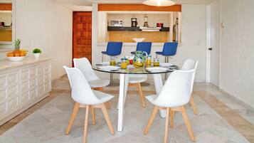 A dining area with a round table, white chairs, and a kitchen in the background.