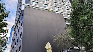 A modern building with a dark facade and multiple windows. There is a sign for a restaurant with outdoor seating visible. - Prestige Skyview Residence – Luxury 2BR • Panoramic Terrace & AC (Warszawa)