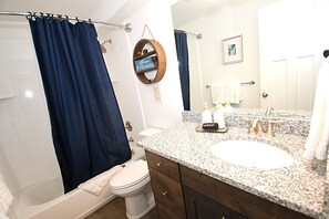 A bathroom with a white toilet, a bathtub, a sink with a granite countertop, and a mirror. - NEW 6BR Bear Lake Home | 2 Min to Beach | Garage, Pool Access, Game Room | Sleeps 18 (Garden City)