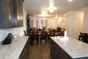A kitchen with granite countertops, wooden cabinets, a dining area with chairs, and a chandelier. - NEW 6BR Bear Lake Home | 2 Min to Beach | Garage, Pool Access, Game Room | Sleeps 18 (Garden City)