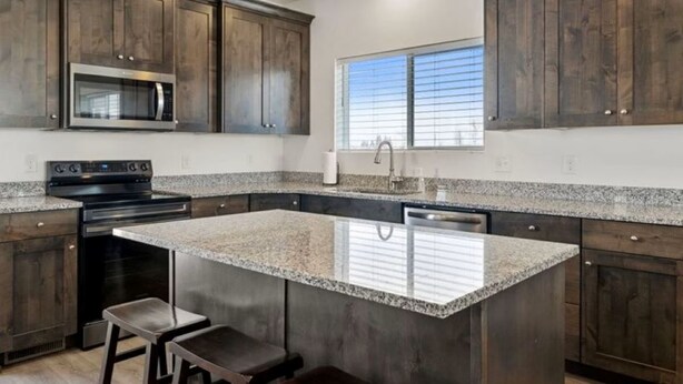 Una cocina con armarios de madera oscura, encimera de granito, electrodomésticos de acero inoxidable y una ventana con persianas.