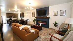 Una sala de estar con sofá, chimenea, televisor y comedor con sillas y mesa.