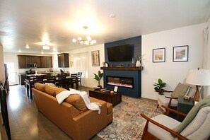 A living room with a sofa, a fireplace, a television, and a dining area with chairs and a table. - NEW 6BR Bear Lake Home | 2 Min to Beach | Garage, Pool Access, Game Room | Sleeps 18 (Garden City)