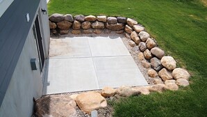 Un patio con borde de piedra, piso de concreto y césped.