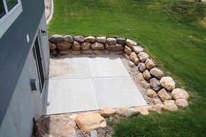 Eine Terrasse mit Steinbord, Betonboden und Rasenfläche.